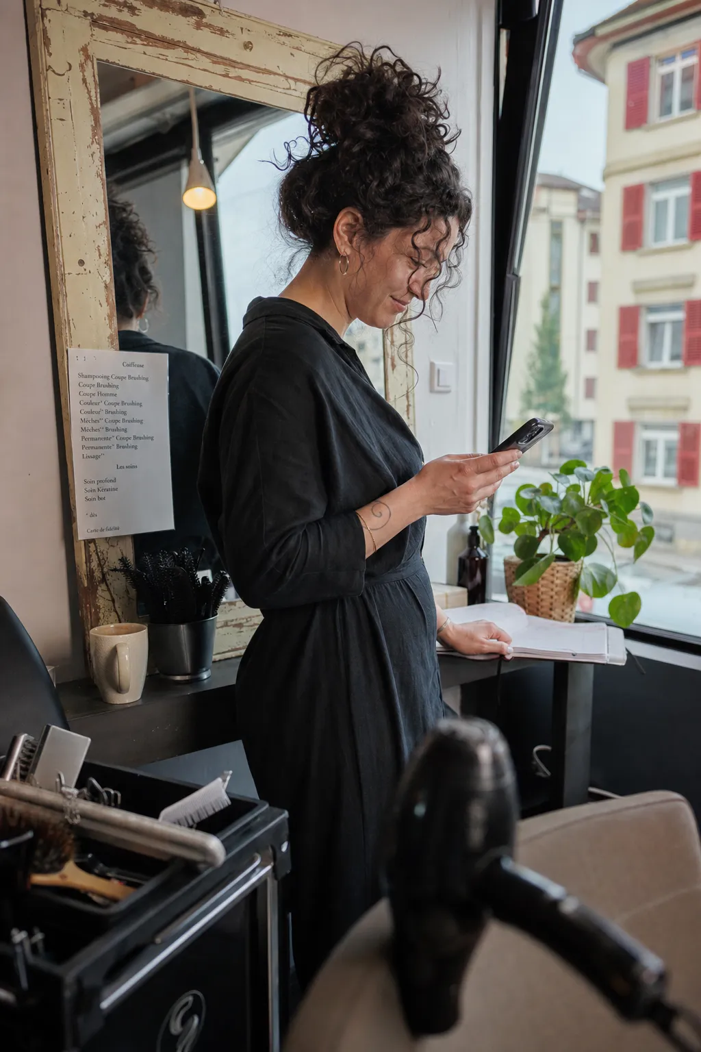 Coiffeuse lisant un message sur son téléphone derrière le comptoir de son salon