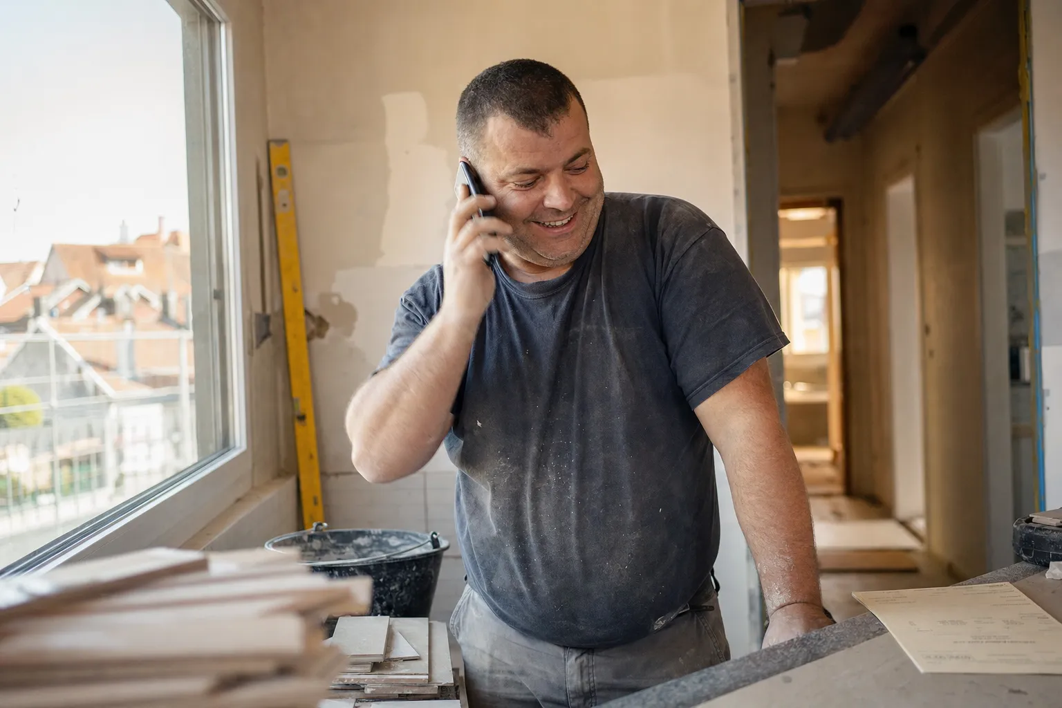 Artisan qui décroche son téléphone en souriant sur un chantier