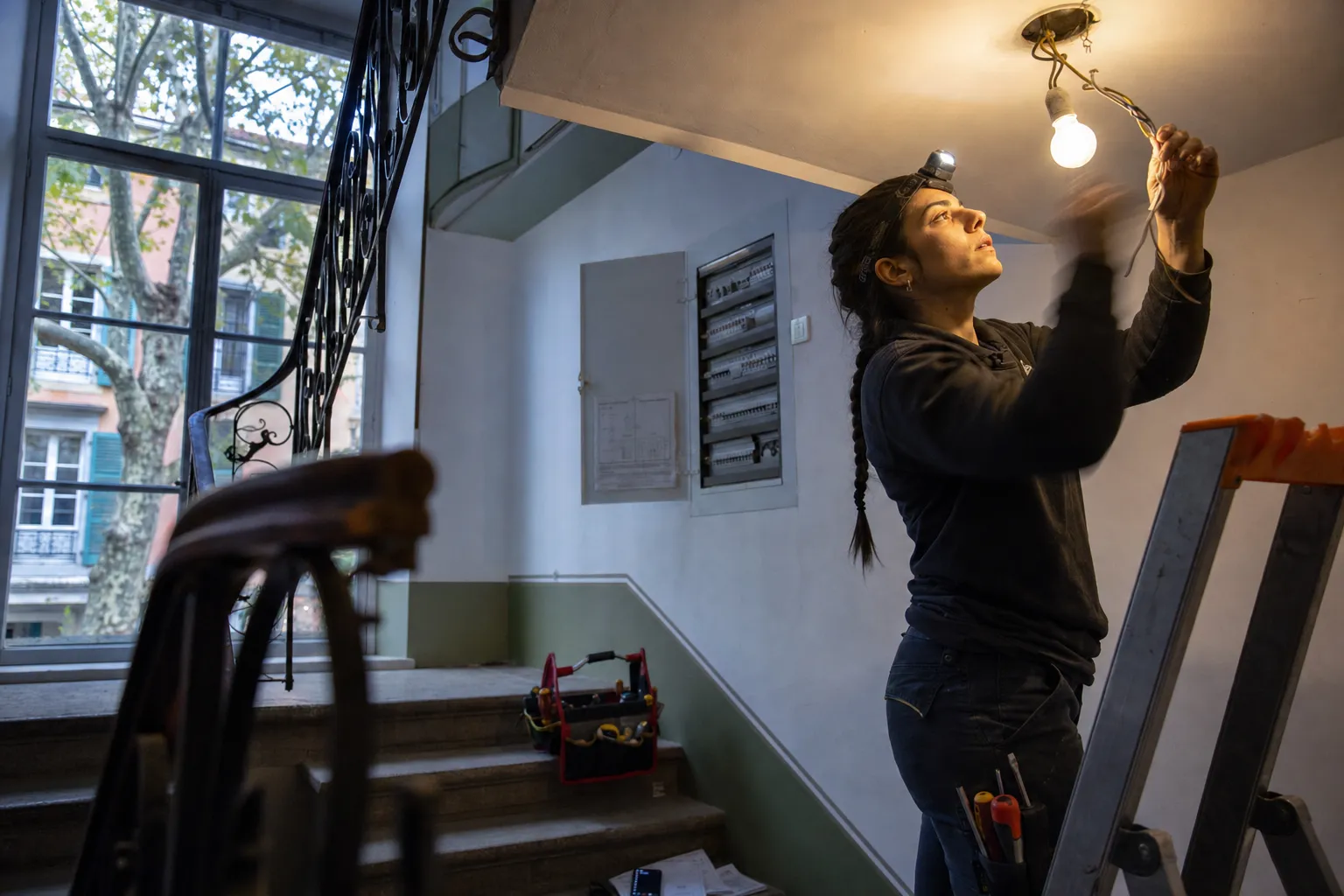 Électricienne sur un escabeau dans une cage d'escalier de Carouge